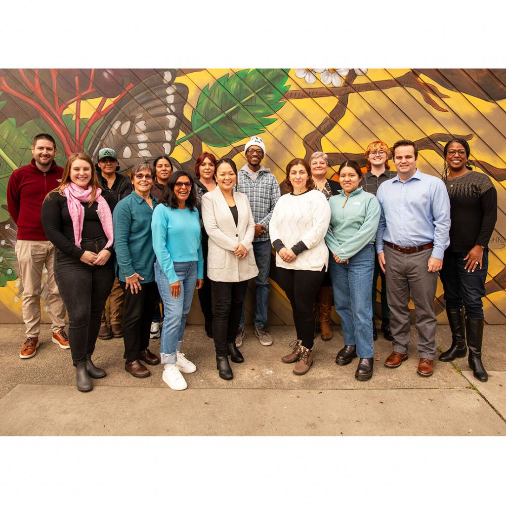 15 people posing for a group photo in front of a mural