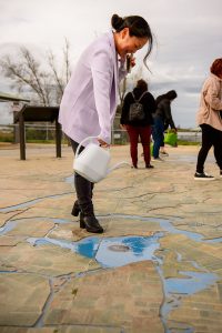 A woman pours water into a concrete map that shows the flow of water in a delta
