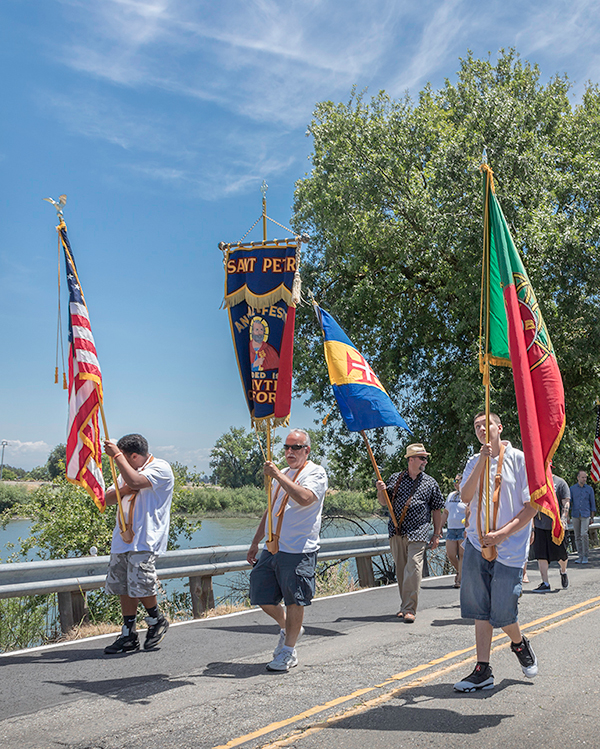 Men carry U.S. and Portuguese flags and a Festa banner in a Festa parade