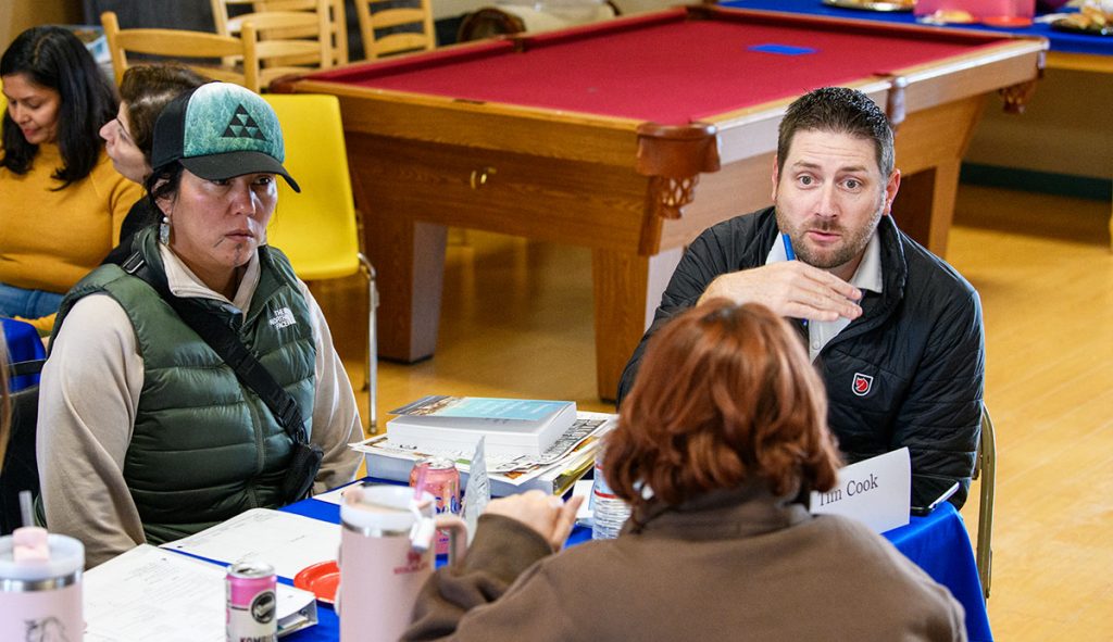 Man and two women talking seriously at a table covered with papers