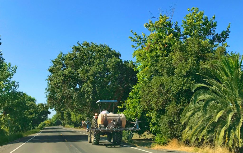 A farm vehicle traveling down a tree-lined country road