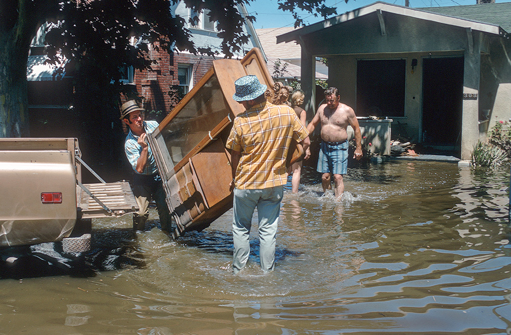 Two men carry a cabinet through flood waters