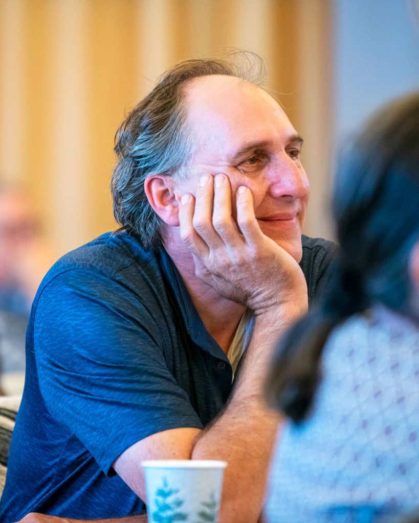 Man with head resting on his hand smiles in reaction to a speaker