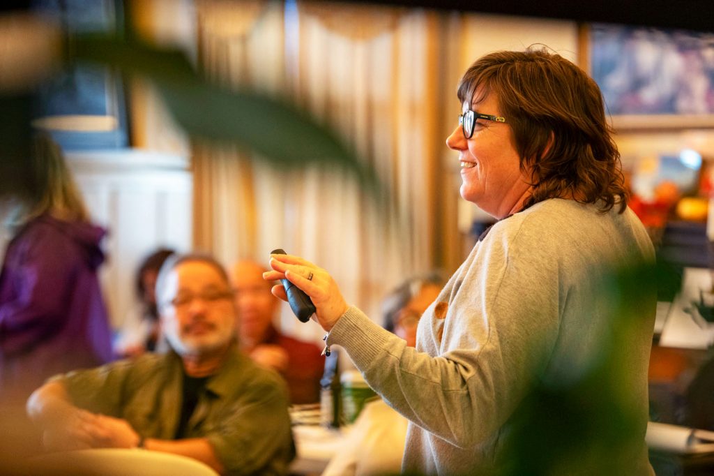 A woman holding a remote control gestures to her audience