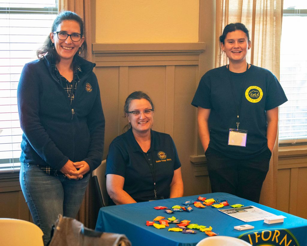 Three women pose for a photo at their information table