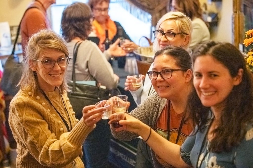 Three women sampling wine raise their glasses to one another