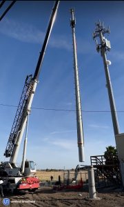 A wireless tower dangles from a crane as it is being installed