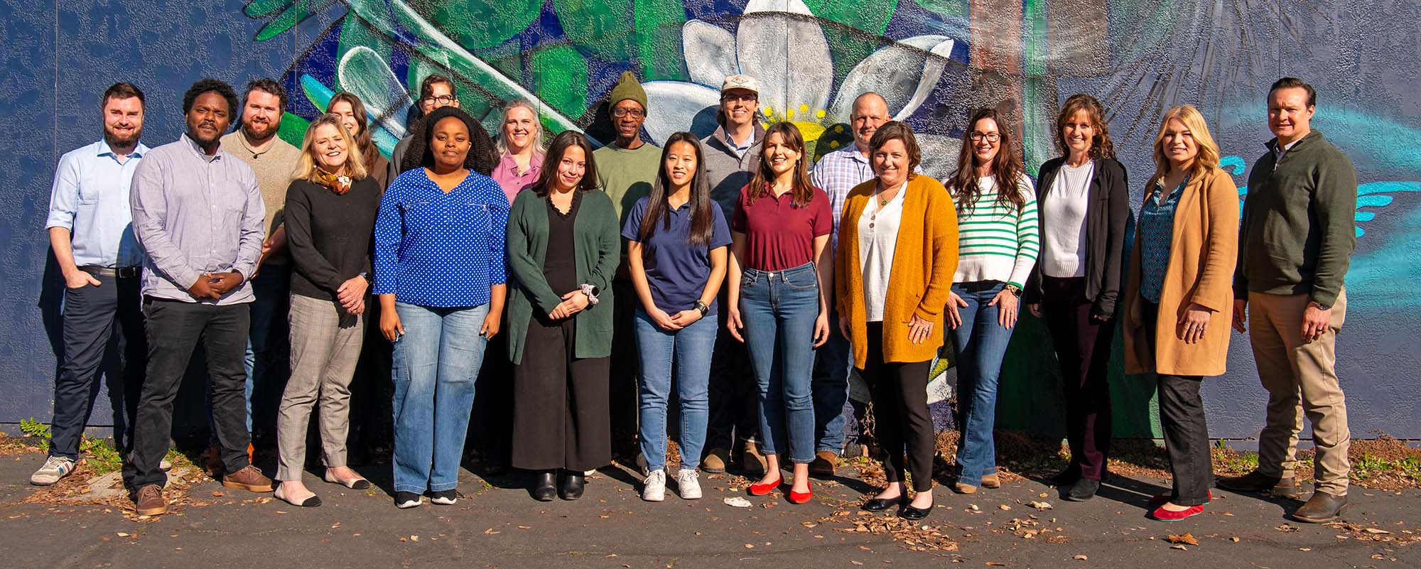 A group of men and women standing in front of a mural posing for the camera