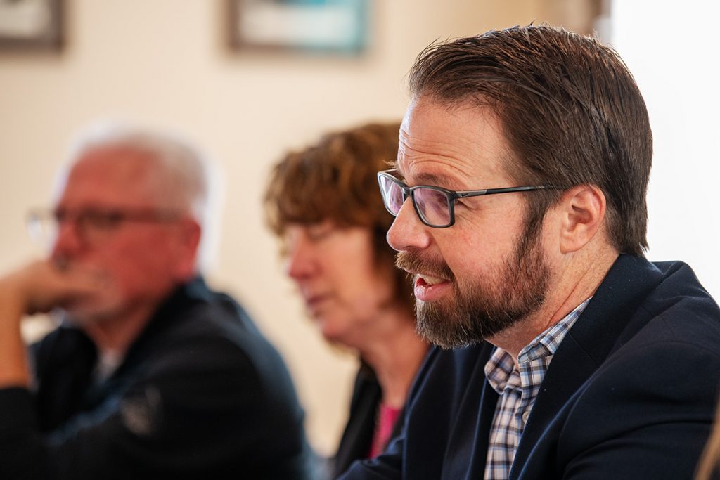 A bearded man speaks, with fellow panelists in the background