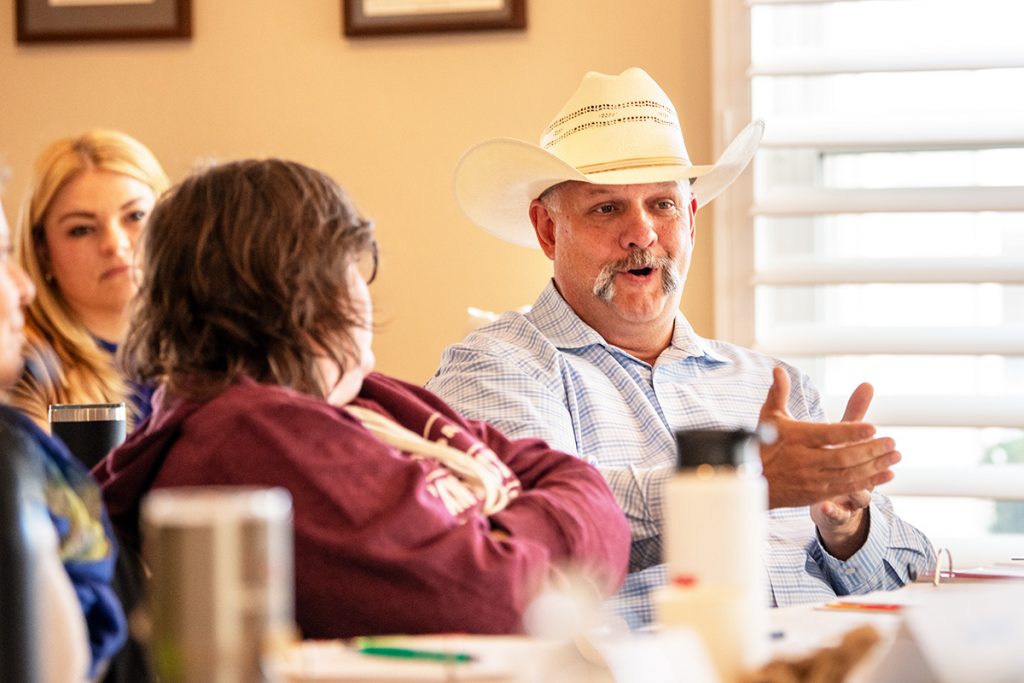 A man in a cowboy hat at a conference table gestures as he speaks