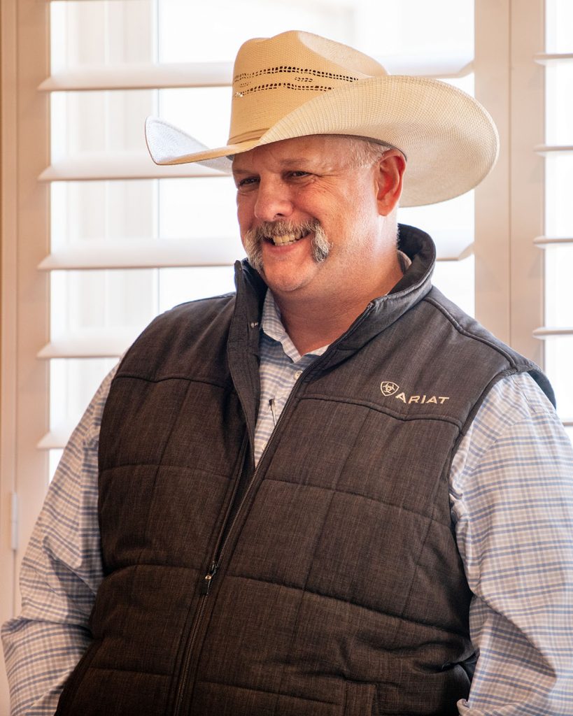 A man in a cowboy hat and vest smiles