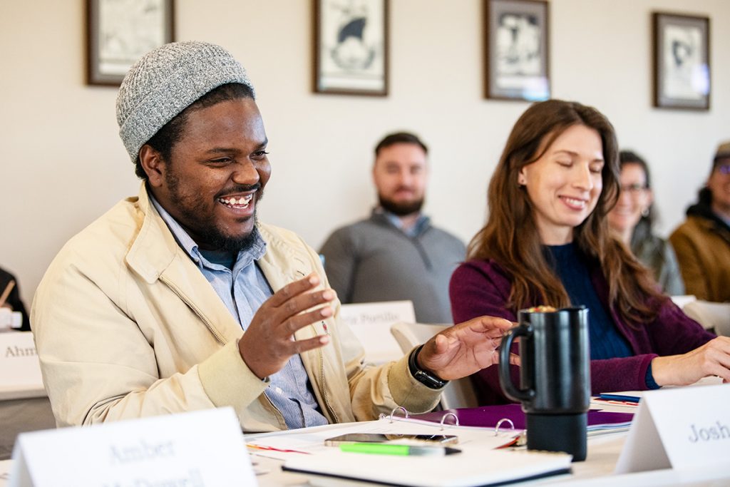 A man at a conference table laughs and gestures