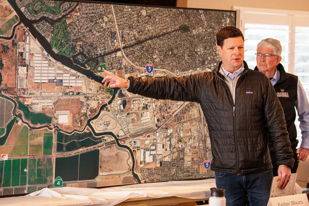 A man gestures at a large map while speaking