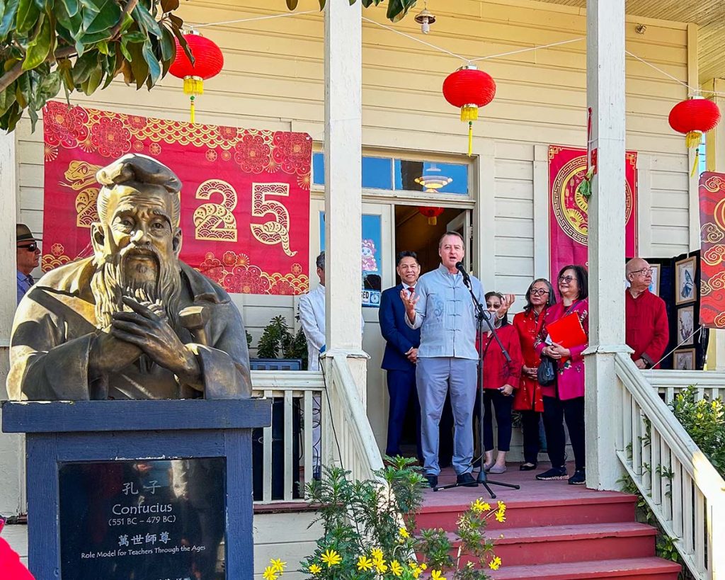 A man speaking at a microphone, with a Confucius bust in the foreground