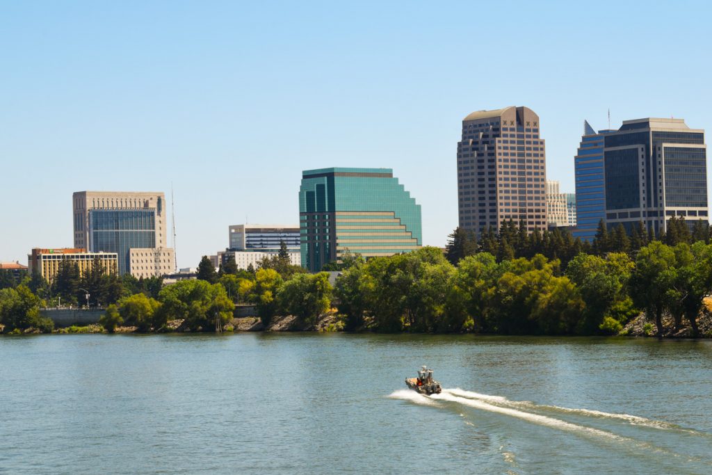 A boat speeds down the Sacramento River with downtown Sacramento in the background