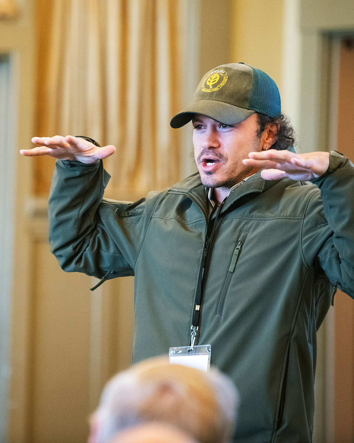 A man with hands out, palms down as he speaks