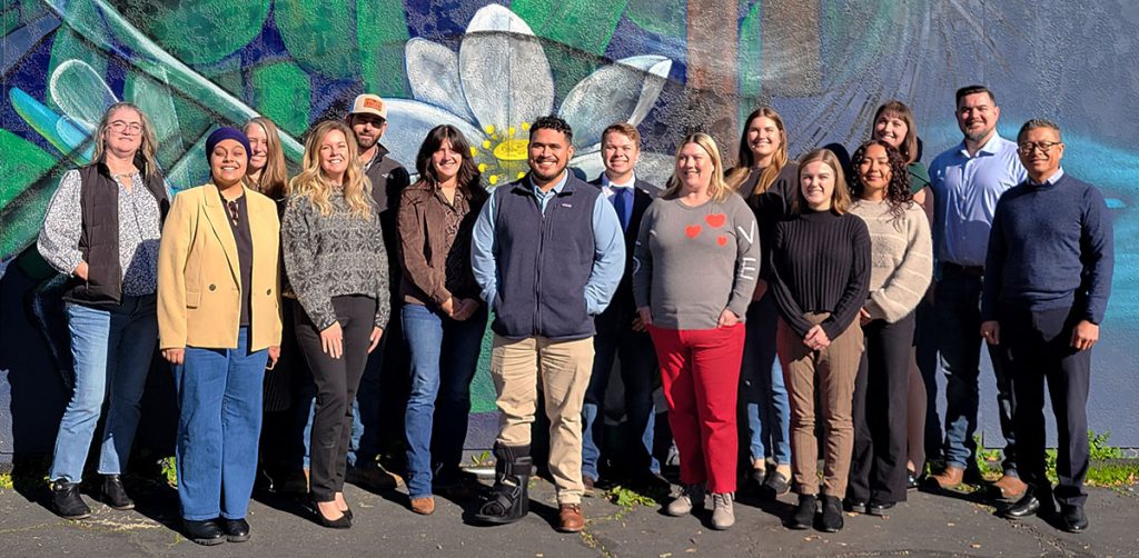 Group photo of adults posing in front of a mural of plant life
