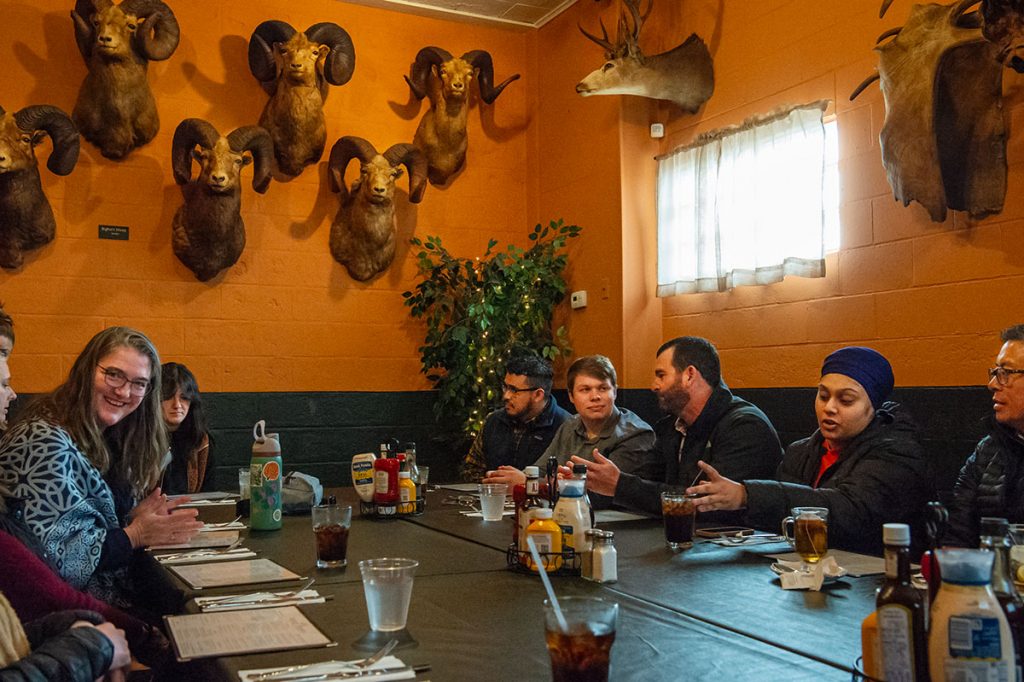 People gathered around a restaurant table with a wall of taxidermied bighorn sheep heads on the wall behind them