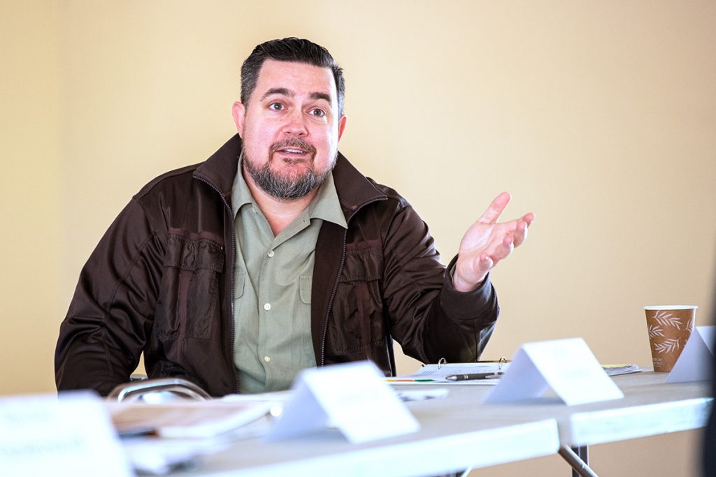 A man at a conference table gestures with his left hand open and facing up