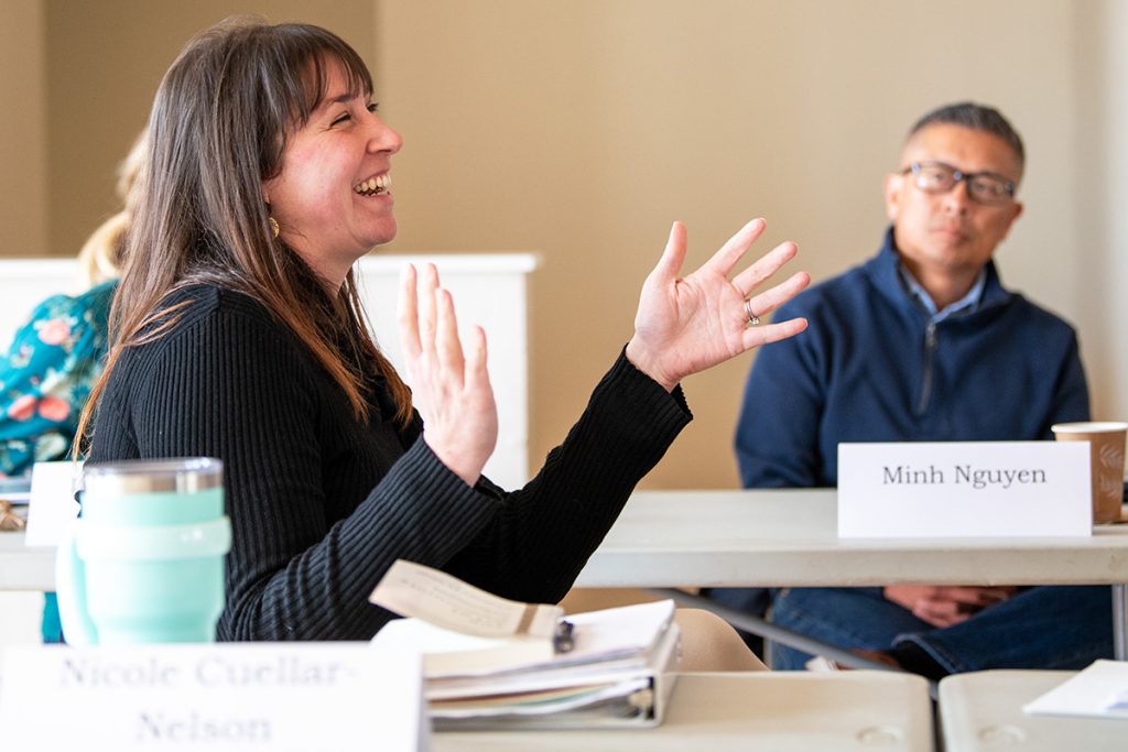 A woman at a conference table laughs as she gestures with open palms
