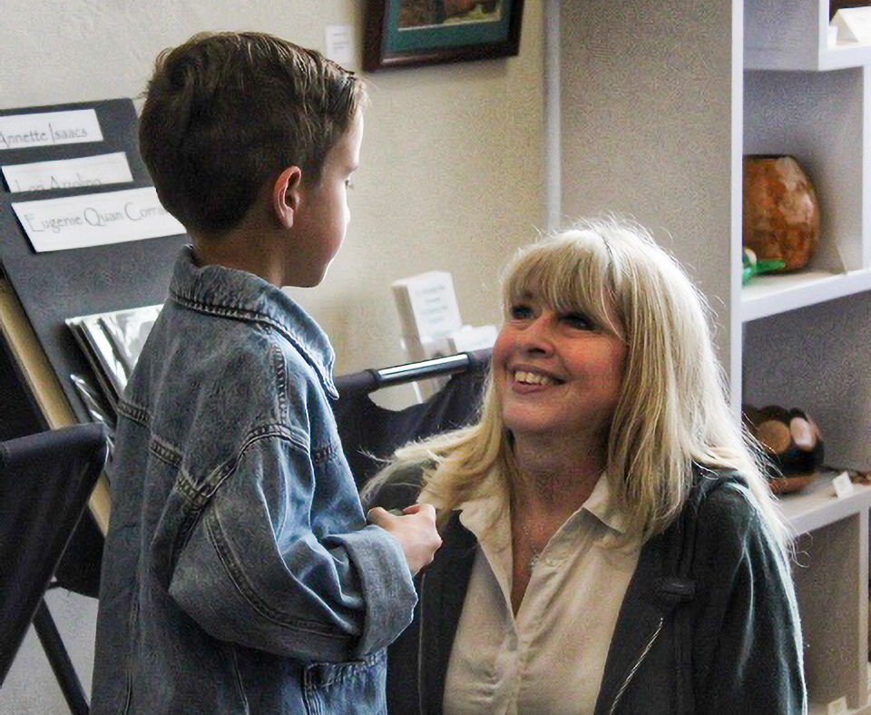 A kneeling woman smiles, looking up at a child's face