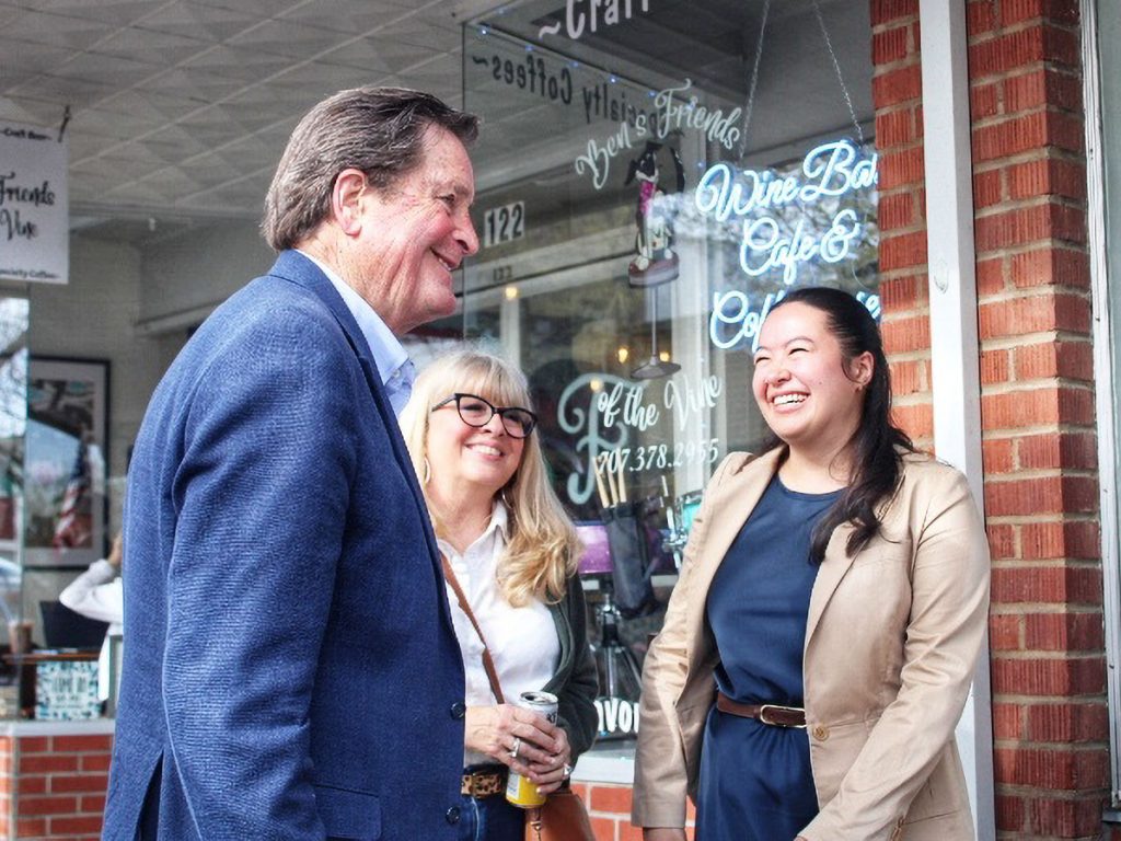 A man chats with two smiling women outside a brick storefront