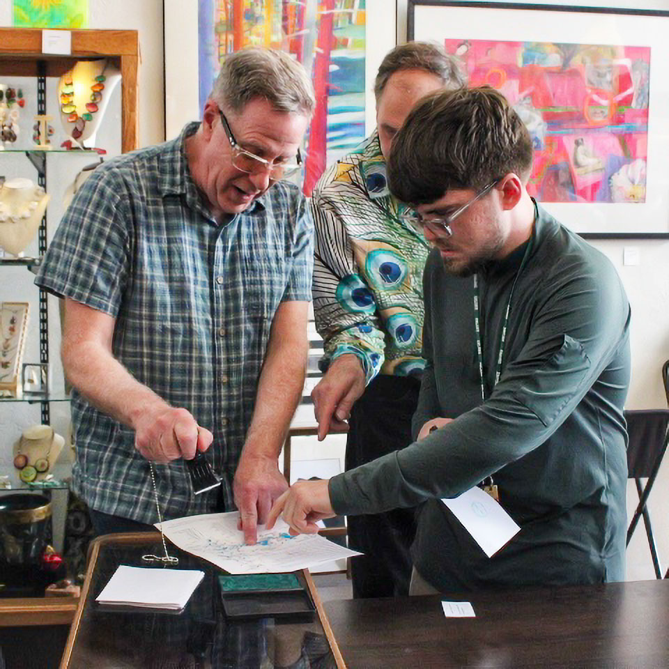Two men point to a location on a map on a piece of paper